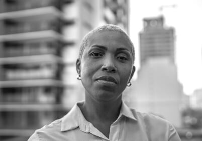 Woman in front of city buildings looking into camera