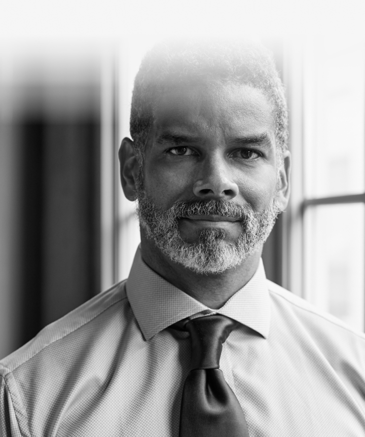 Man wearing dress shirt and tie leaning on window and looking into camera