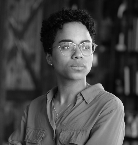 Woman wearing blouse and glasses standing in front of bookshelf and looking into the distance