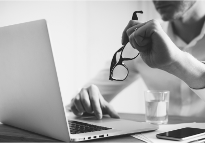 Man looking at laptop and holding glasses between his fingers